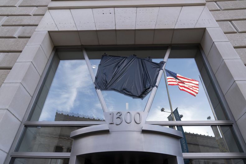 La bandera estadounidense ondea junto a un asta bandera vacía que previamente tenía la bandera de la Agencia de Estados Unidos para el Desarrollo Internacional (USAID, por sus siglas en inglés), vistas en el reflejo de un cristal en el que anteriormente estaban el letrero y el sello de USAID, el viernes 7 de febrero de 2025, afuera de la sede de la agencia en Washington. (AP Foto/José Luis Magaña)