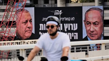 Un hombre en bicicleta pasa por delante de un anuncio de una cadena de televisión con la imagen del primer ministro de Israel, Benjamin Netanyahu (derecha), y su principal rival, el candidato opositor Gadi Eisenkot, antes de las elecciones generales en el país, en Ramat Gan, Israel, el 23 de septiembre de 2026. (AP Foto/Oded Balilty)