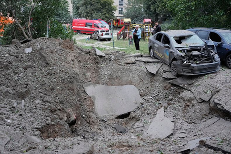 Residentes locales permanecen cerca de un cráter y de automóviles dañados por un ataque con misiles rusos en Kiev, Ucrania, el lunes 6 de julio de 2026. (Foto AP/Efrem Lukatsky)