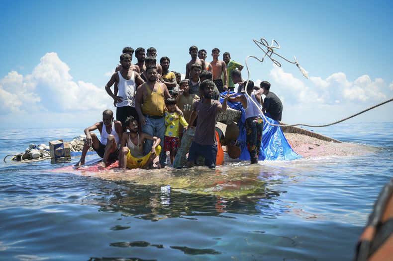 Refugiados rohinya, en pie sobre su embarcación volcada mientras los rescatistas les lanzan una cuerda, en Aceh Occidental, Indonesia, el 21 de marzo de 2024. (AP Foto/Reza Saifullah)