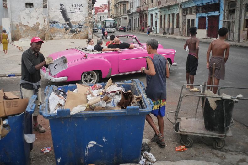 Un hombre recoge basura mientras los turistas viajan en un automóvil clásico estadounidense durante un apagón en La Habana, Cuba, el miércoles 3 de diciembre de 2025. (AP Foto/Ramón Espinosa)