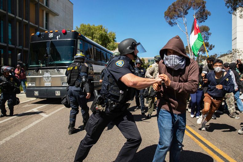 Un agente de la policía del campus de la Universidad de California aparta a un manifestante propalestino de un autobús del jefe policial de San Diego que transportaba a manifestantes arrestados en la UC en San Diego, el 6 de mayo de 2024, en San Diego. (Adriana Heldiz/CalMatters vía AP)