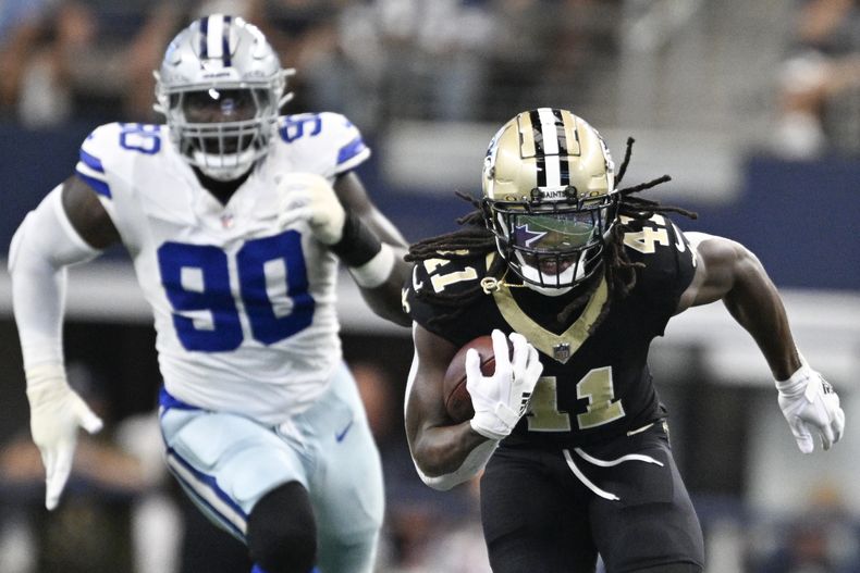 Alvin Kamara (41), running back de los Saints de Nueva Orleans, se escapa ante la mirada lejana de DeMarcus Lawrence (90), defensive end, en camino a una anotación en espectacular escapada en la primera mitad del juego de la NFL, el domingo 15 de septiembre de 2024, en Arlington, Texas. (AP Foto/Tony Gutierrez)