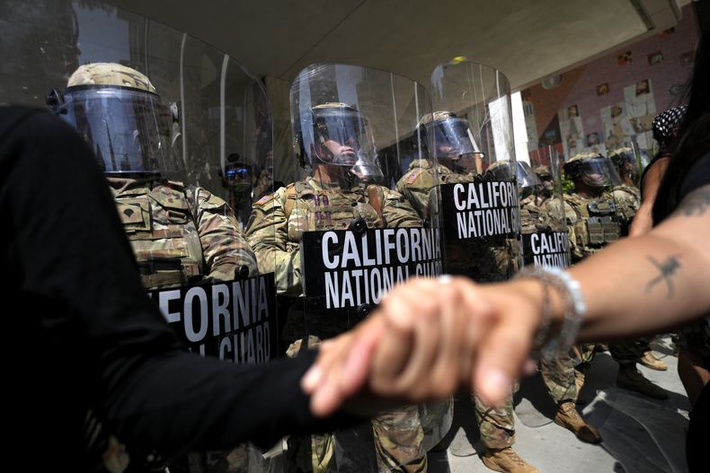 Manifestantes se toman de las manos frente a soldados de la Guardia Nacional de California el lunes 9 de junio de 2025, en un edificio federal en el centro de Los Ángeles. (AP Foto/Jae Hong)