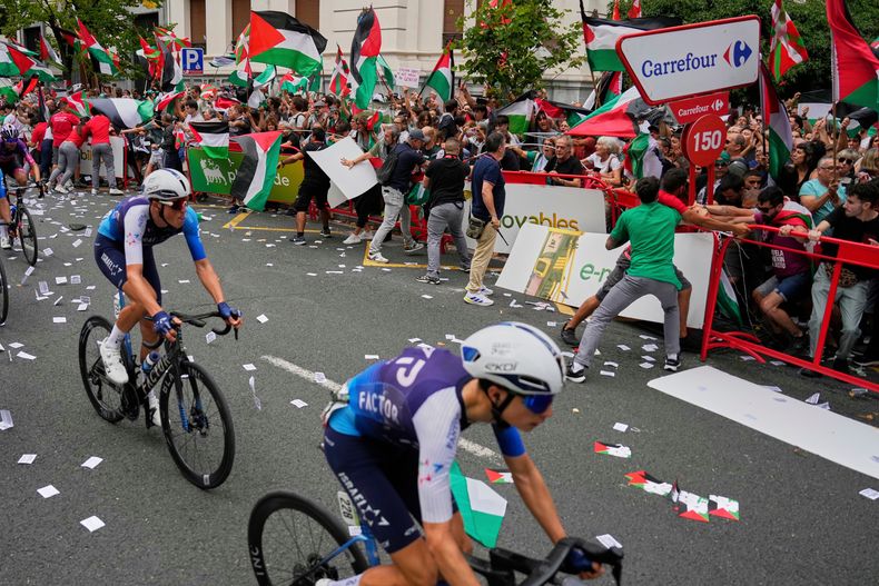 ARCHIVO - Ciclistas del equipo Israel Premier Tech compiten mientras personas con banderas Palestinas intentan interrumpir la undécima etapa de la carrera ciclista de la Vuelta Española, de Bilbao a Bilbao, España, el miércoles 3 de septiembre de 2025. (AP Photo/Miguel Oses, Archivo)
