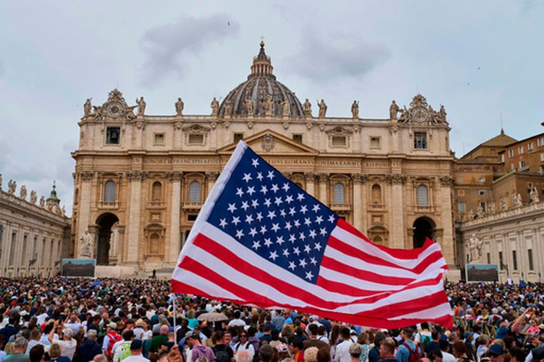 ARCHIVO - Una bandera estadounidense ondea entre la multitud mientras el papa León XIV aparece en el balcón central de la basílica de San Pedro para su primera bendición dominical tras su elección, en la plaza de San Pedro del Vaticano, el 11 de mayo de 2025. (AP Foto/Bernat Armangue, archivo)