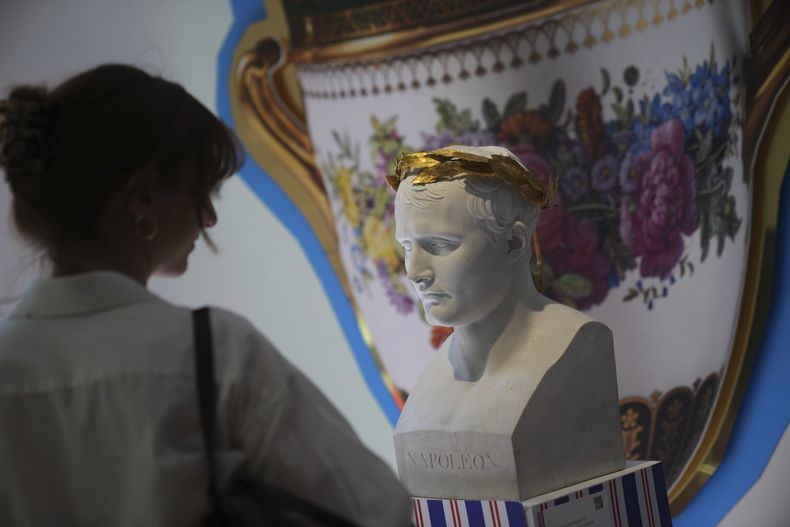 Una mujer observa un busto de Napoleón en una exposición de pertenencias de Napoleón creada por el diseñador francés Jean-Charles de Castelbajac en la casa de subastas Sothebys en París el jueves 19 de junio de 2025 en París. (Foto AP/Christophe Ena)