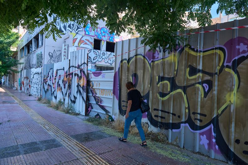 Una mujer camina frente al edificio abandonado donde se encontró el cuerpo de la escocesa Elisabeth Jane Ross dentro de una maleta, en Atenas, Grecia, el miércoles 5 de agosto de 2026. (AP Foto/Petros Giannakouris)