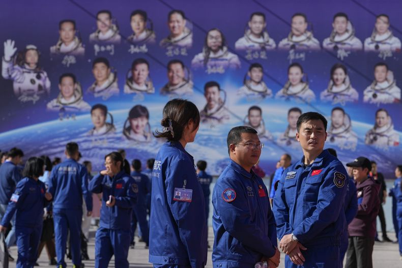 Trabajadores reunidos cerca de un cartel que muestra a astronautas chinos de misiones pasadas de Shenzhou, después de que astronautas de la próxima misión Shenzhou-17 con la prensa en el Centro de Lanzamiento de Satélites Jiuquan en el noroeste de China, el miércoles 25 de octubre de 2023. (AP Foto/Andy Wong)