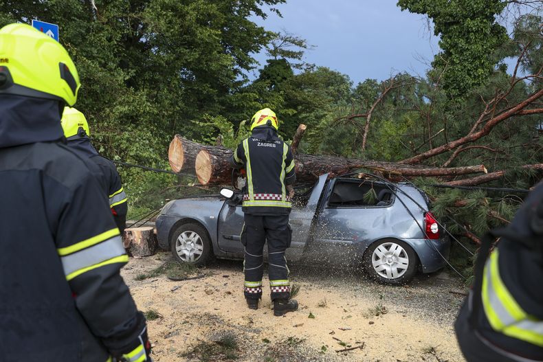 Bomberos retiran ramas de un árbol caído sobre un auto dañado, luego de una potente tormenta en Zagreb, Croacia, el 19 de julio de 2023. (AP Foto)