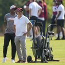 Josh Harris, derecha, nuevo dueño de los Commanders de Washington, sonríe con el legendario Joe Theismann, izquierda, Mitchell Rales, y otros, durante el entrenamiento del equipo en las instalaciones, el miércoles 26 de julio de 2023, en Ashburn, Virginia. (AP Foto/Alex Brandon)