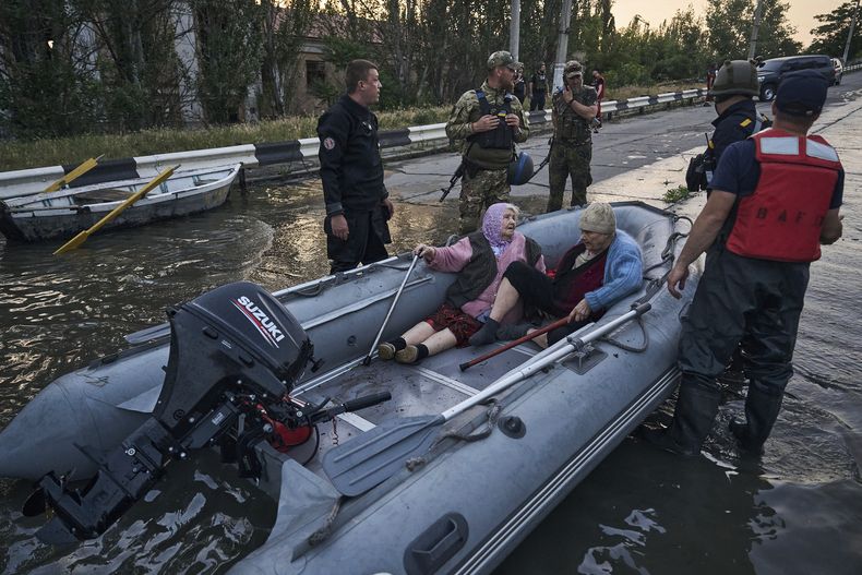 Rescatistas intentan remolcar dos botes que llevan a residentes evacuados de un vecindario inundado, el martes 6 de junio de 2023, en Jersón, Ucrania. (AP Foto/Libkos)