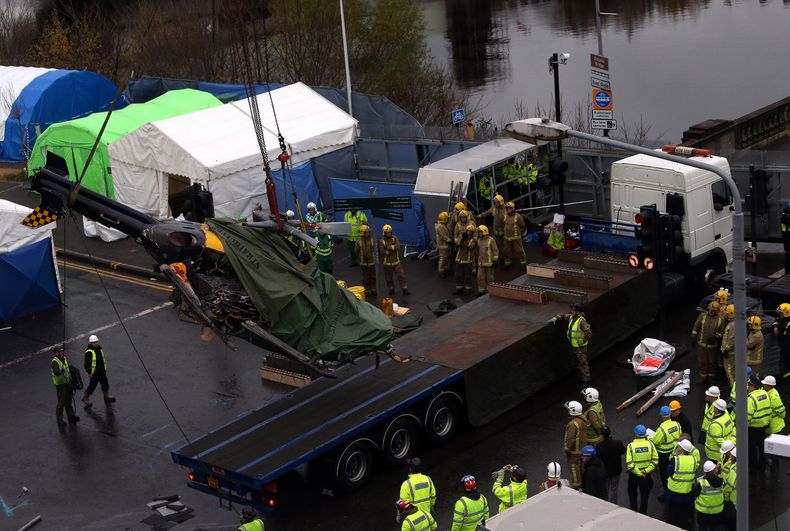 Personal de bomberos obsreva c&oacute;mo un helic&oacute;ptero accidentado es elevado para colocar en un remolque despues que el aparato se precipit&oacute; sobre un bar de Glasgow con un saldo de 9 muertos, el lunes 2 de diciembre del 2013. (AP Foto)