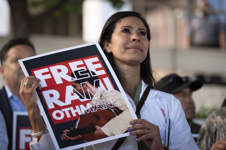 La doctora Wafaa Alrashid, al centro, cuyo esposo Rami Othmane, un músico tunecino, está detenido en una instalación del Servicio de Inmigración y Control de Aduanas, sostiene un letrero durante un mitin frente a ese lugar, el viernes 25 de julio de 2025, en Los Ángeles. (AP Foto/Jae C. Hong)