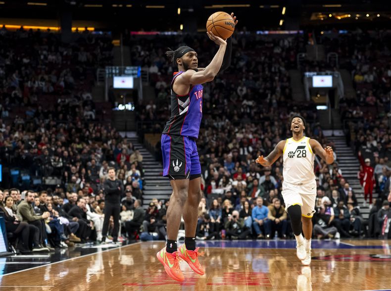 Immanuel Quickley (5), de los Raptors de Toronto, dispara desde larga distancia mientras Brice Sensabaugh (28), del Jazz de Utah, intenta distraerlo durante la segunda mitad del juego de baloncesto de la NBA, el viernes 7 de marzo de 2025, en Toronto. (Christopher Katsarov/The Canadian Press vía AP)