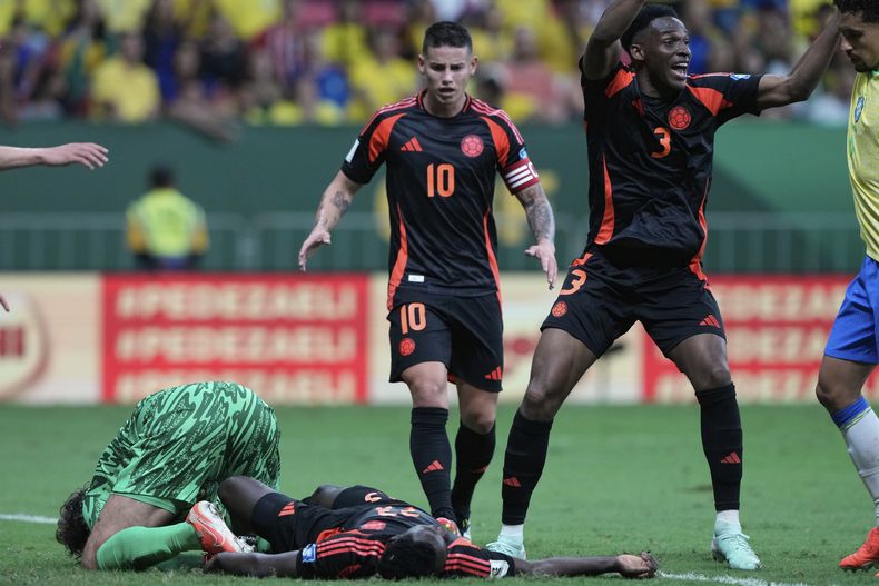 El arquero brasileño Alisson (izquierda) y el zaguero colombiano Davinson Sánchez quedan en el piso tras un choque de cabezas en el partido por las eliminatorias del Mundial, el jueves 20 de marzo de 2025, en Brasilia. (AP Foto/Eraldo Peres)