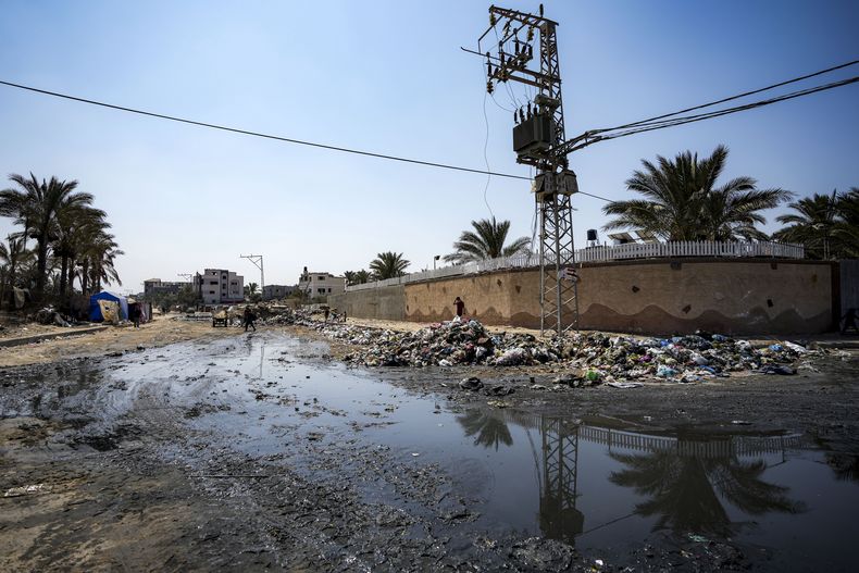 Palestinos desplazados por la ofensiva aérea y terrestre israelí sobre la Franja de Gaza caminan junto a un turbio reguero de aguas residuales que fluye por las calles de Deir al-Balah, en el centro de la Franja de Gaza, el martes 27 de agosto de 2024. (Foto AP/Abdel Kareem Hana)