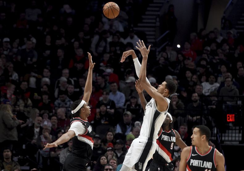 El francés Victor Wembanyama, de los Spurs de San Antonio, dispara entre Moses Brown (izquierda) y Jerami Grant (derecha, atrás), de los Trail Blazers de Portland, durante el encuentro del jueves 28 de diciembre de 2023 (AP Foto/Steve Dykes)