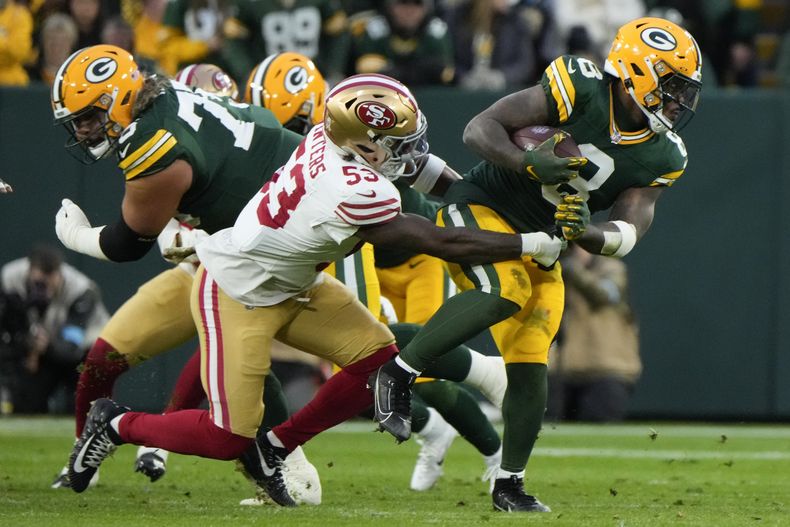 Josh Jacobs (8), running back de los Packers de Green Bay, corre con el balón, e intenta romper un derribo de Dee Winters (53), linebacker de los 49ers de San Francisco, durante la primera mitad del partido de la NFL del domingo 24 de noviembre de 2024, en Green Bay, Wisconsin. (AP Foto/Morry Gash)