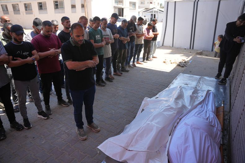 Personas rezan ante los cuerpos de hombres palestinos que murieron en un ataque aéreo israelí en el campo de refugiados de Maghazi el viernes, durante su funeral en Deir al-Balah, Franja de Gaza, el sábado 27 de junio de 2026. (Foto AP/Abdel Kareem Hana)