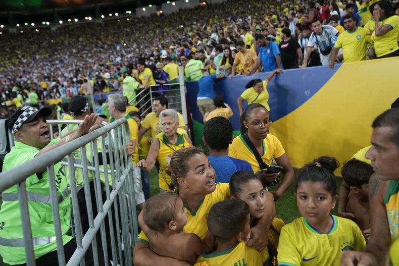 Una mujer trata de proteger a sus hijos de una riña entre hinchas, antes del partido entre Brasil y Argentina, el martes 21 de noviembre de 2023, en el Maracaná de Río de Janeiro (AP Foto/Silvia Izquierdo)