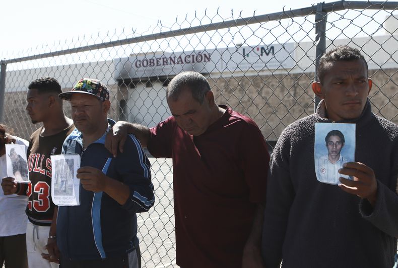 ARCHIVO - Migrantes, principalmente de Venezuela, muestran fotos de quienes murieron en un incendio en el centro de detención de migrantes mexicano detrás de ellos, durante una vigilia de oración a las afueras del mismo en Ciudad Juárez, México, el 27 de abril de 2023. Cuatro meses después del incendio en un centro de detención de migrantes de la frontera en el que murieron 40 personas, varios supervivientes siguen viviendo en el limbo en un hotel de Ciudad de México, mientras se recuperan de las heridas y en espera de que los responsables sean procesados. (AP Foto/Christian Chávez, Archivo)