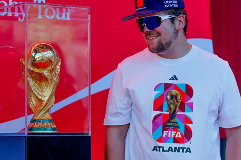 Joseph Pozdnakov se saca una foto con el trofeo del Mundial de fútbol previo a un juego de béisbol entre los Bravos de Atlanta y los Cachorros de Chicago, el 14 de mayo de 2026, en Atlanta. (AP Foto/Erik S. Lesser)