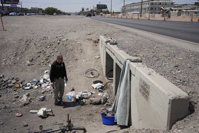 Mark Paulson, un funcionario local, sostiene latas de agua fría mientras revisa un campamento para indigentes, el miércoles 10 de julio de 2024, en Henderson, Nevada. (AP Foto/John Locher)
