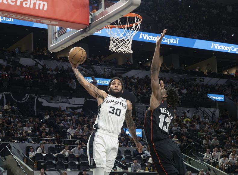 El alero de los Spurs de San Antonio, Julian Champagnie (30), realiza una volcada contra el pívot de Detroit James Wiseman (13) durante la primera mitad del partido de baloncesto de la NBA, el domingo 14 de abril de 2024, en San Antonio. (AP Foto/Michael Thomas)