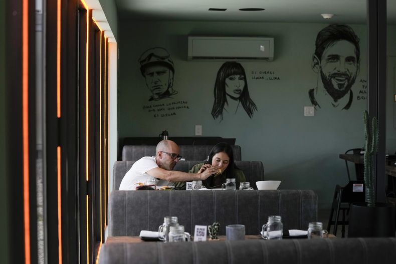 Una pareja come cerca de murales de celebridades, incluido el futbolista argentino Lionel Messi, en el Kao Bar & Grill de Hallandale Beach, Florida, el lunes 10 de julio de 2023 (AP Foto/Rebecca Blackwell)