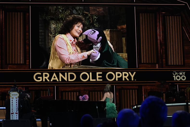 Un video de Loretta Lynn y el Conde von Count de Sesame Street es proyectado mientras las marionetas Abby Cadabby y Tayla Lynn, abajo, actúan en el Grand Ole Opry, el jueves 14 de agosto de 2025, en Nashville, Tennessee. (Foto AP/George Walker IV)