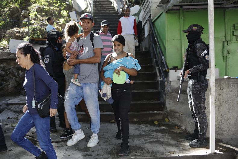 Residentes pasan junto a la Policía Nacional Bolivariana en el área de Petare en Caracas, Venezuela, el miércoles 22 de enero de 2025, después de que el gobierno anunciara la muerte del líder de la pandilla Wilexis, Wuileisys Alexander Acevedo Monasterio. (AP Foto/Cristian Hernández)