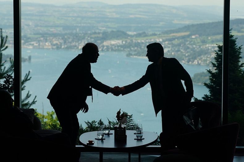 Delegados se saludan en el recibidor en el primer día de un encuentro a cuatro bandas entre Estados Unidos, Irán, Pakistán y Qatar, en el Buergenstock Resort Lake Lucerne, cerca de Stansstad, Suiza, el 21 de junio de 2026. (Nathan Howard/Pool Foto vía AP)