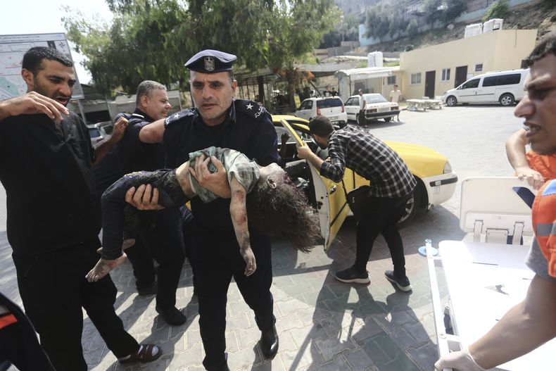 Un policía de Hamas llega con una niña herida a un hospital el domingo 8 de octubre de 2023, en Beit Lahiya, en la Franja de Gaza. (AP Foto/Mahmoud Essa)
