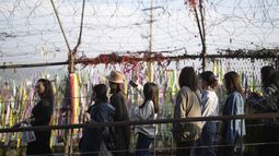 Visitantes caminan cerca de una cerca decorada con lazos con mensajes deseando la reunificación de las dos Coreas en el Pabellón Imjingak en Paju, Corea del Sur, el jueves 31 de octubre de 2024. (AP Foto/Lee Jin-man)