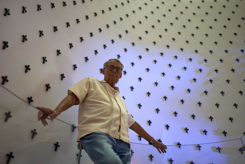 Fabián Escalante Font, exjefe de la seguridad del Estado cubano, posa para una foto frente a un mural de cruces que representan a las víctimas del terrorismo contra Cuba en el Memorial de la Denuncia en La Habana, el martes 8 de abril de 2025. (AP Foto/Ramón Espinosa)