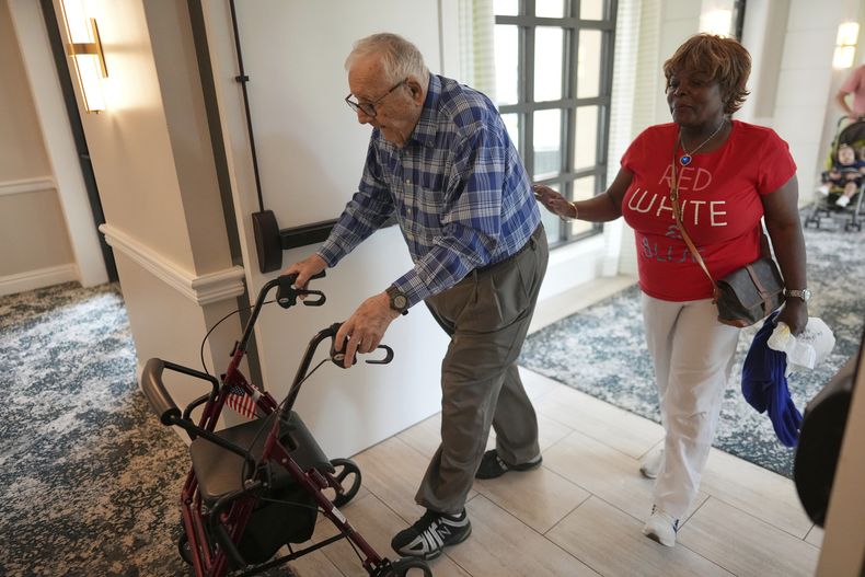 Eugene Preslier, derecha, es acompañado por su enfermera privada certificada Miriam Louis al volver a su apartamento desde el comedor, en la residencia de ancianos Toby and Leon Cooperman Sinai Residences, el 4 de julio de 2025, en Boca Raton, Florida. (AP Foto/Rebecca Blackwell)