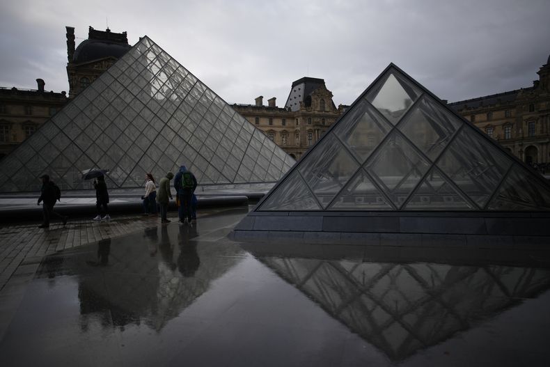 Varias personas pasean por el patio del museo del Louvre bajo la lluvia, en París, el 27 de octubre de 2025s. (AP Foto/Christophe Ena)