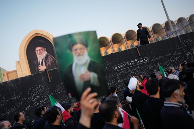 Una persona sostiene un retrato del fallecido líder supremo de Irán, el ayatolá Alí Jamenei, mientras pasa junto a un muro con mensajes, incluido uno en inglés que dice Mataremos a Trump, durante los actos fúnebres por Jamenei y miembros de su familia en la Gran Mezquita Imán Jomeini en Teherán, Irán, el sábado 4 de julio de 2026. (AP Foto/Altaf Qadri)