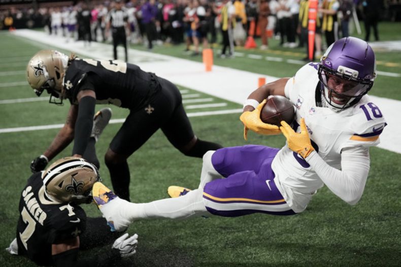 El receptor abierto de los Vikings de Minnesota, Justin Jefferson (18), atrapa un pase de touchdown ante el safety de los Saints de Nueva Orleans, Jonas Sanker (7), y el esquinero Quincy Riley durante la segunda mitad de un partido de fútbol americano de la NFL en Nueva Orleans, el domingo 11 de octubre de 2026. (Foto AP/Matthew Hinton)