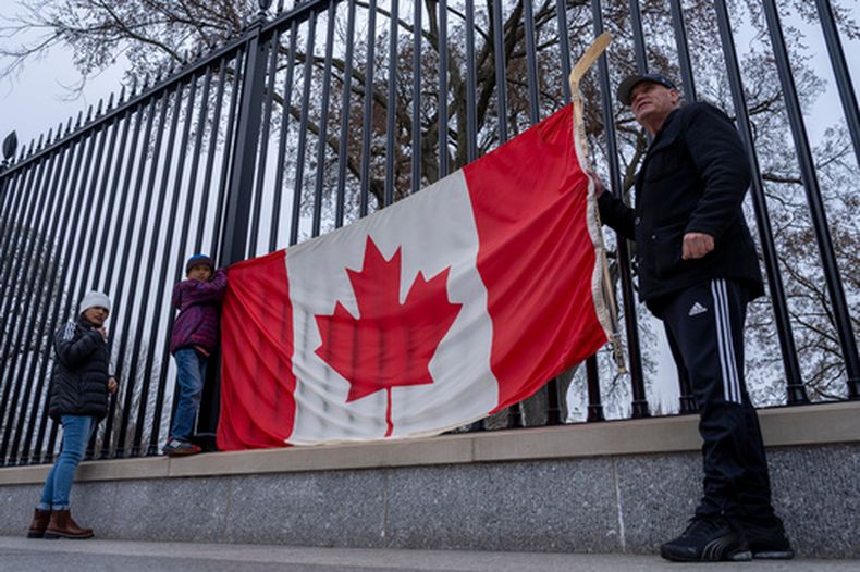 ARCHIVO - De derecha a izquierda, los residentes de Toronto Douglas Bloomfield, su hijo Phoenix y su esposa Ame, quienes se encuentran de vacaciones en Washington, sostienen una bandera canadiense y un palo de hockey sobre hielo para mostrar su apoyo a Canadá en relación con los aranceles comerciales, frente a la Casa Blanca en Washington, el 13 de marzo de 2025. (AP Foto/Ben Curtis/Archivo)
