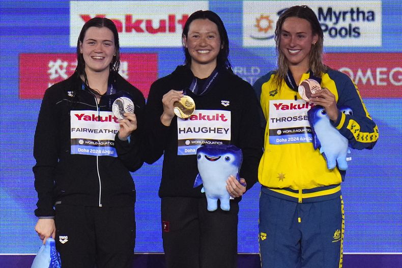 Siobhan Bernadette Haughey de Hong Kong sostiene su medalla tras ganar el Campeonato Mundial de Natación en Doha junto a la medallista de plata, la neozelandesa Erika Fairweather y la australiana Brianna Throssell el 14 de febrero del 2024. (AP Foto/Hassan Ammar)