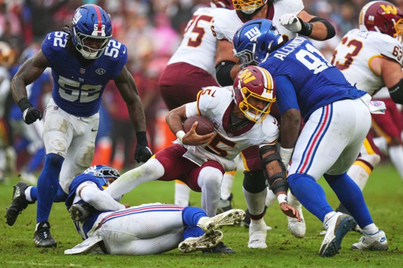 Dru Phillips (22), de los Giants de Nueva York, derriba al quarterback Jayden Daniels (5), de los Commanders de Washington, mientras corría para superar a Darius Alexander (91) y Arvell Reese (52) durante la segunda mitad del partido de la NFL, el domingo 11 de octubre de 2026, en in Landover, Maryland. (AP Foto/Stephanie Scarbrough)