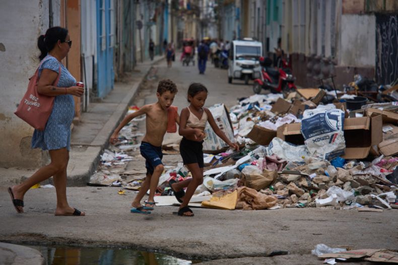 Niños corren junto a un montón de basura acumulada en una calle durante un apagón en La Habana, Cuba, el lunes 6 de julio de 2026. (Foto AP/Ramón Espinosa)