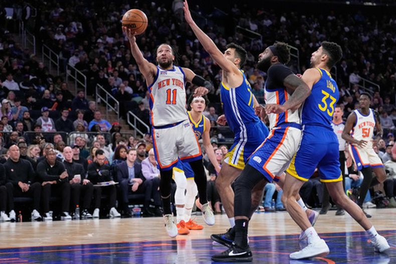 Jalen Brunson (11), izquierda, de los Knicks de Nueva York, se enfila a la canasta para encestar pasando a jugadores de los Warriors de Golden State durante la segunda mitad del partido de baloncesto de la NBA, el domingo 15 de marzo de 2026, en Nueva York. (AP Foto/Seth Wenig)