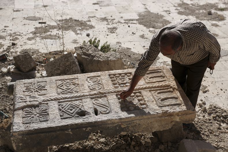 Un guardia inspecciona una piedra tallada, hallada originalmente en un complejo de tumbas subterráneas bizantinas que se cree tienen más de 1.500 años de antigüedad y fueron reveladas por un contratista durante la reconstrucción de una casa destruida en un ataque y que ahora se encuentra en el patio de un museo en Maarat al-Numan, Siria, el viernes 30 de mayo de 2025. (AP Foto/Omar Albam)