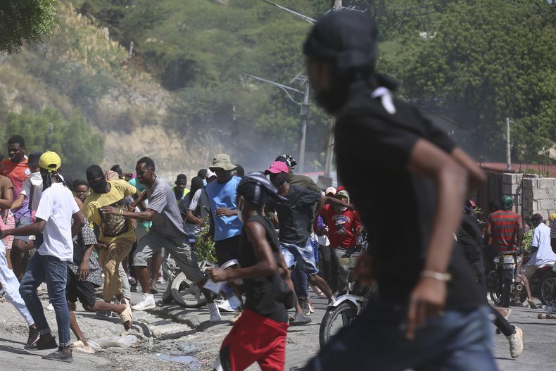 Un grupo de personas huye del gas lacrimógeno disparado por la policía para dispersar a los manifestantes que exigen a la policía y al primer ministro que actúen de inmediato contra las pandillas, en Puerto Príncipe, Haití, el lunes 19 de agosto de 2024. (AP Foto/Odelyn Joseph)