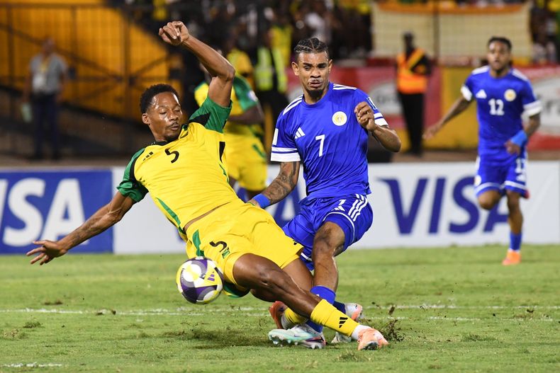 Juninho Bacuna, de Curazao, al centro, lucha por el balón contra Ethan Pinnock, de Jamaica, a la izquierda, durante un juego de fútbol de clasificación para la Copa del Mundo de 2026 en Kingston, Jamaica, el martes 18 de noviembre de 2025. (AP Photo/Collin Reid)