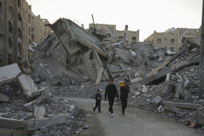 Jóvenes palestinos caminan entre los escombros de edificios destruidos en un vecindario en Jan Yunis, Gaza, el 1 de diciembre de 2024. (AP Foto/Abdel Kareem Hana)
