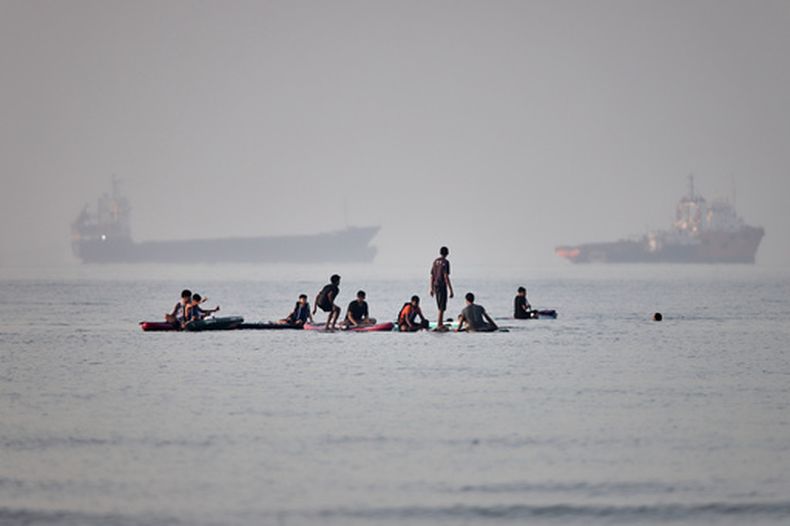 Varias personas se congregan en tablas de remo en aguas poco profundas al tiempo que buques de carga y de servicio permanecen anclados en el estrecho de Ormuz, frente a Bandar Abbas, Irán, el lunes 1 de junio de 2026. (Amirhosein Khorgooi/ISNA vía AP)